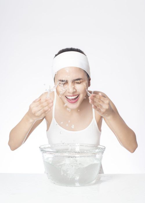 Beautiful woman is washing her face on white background
